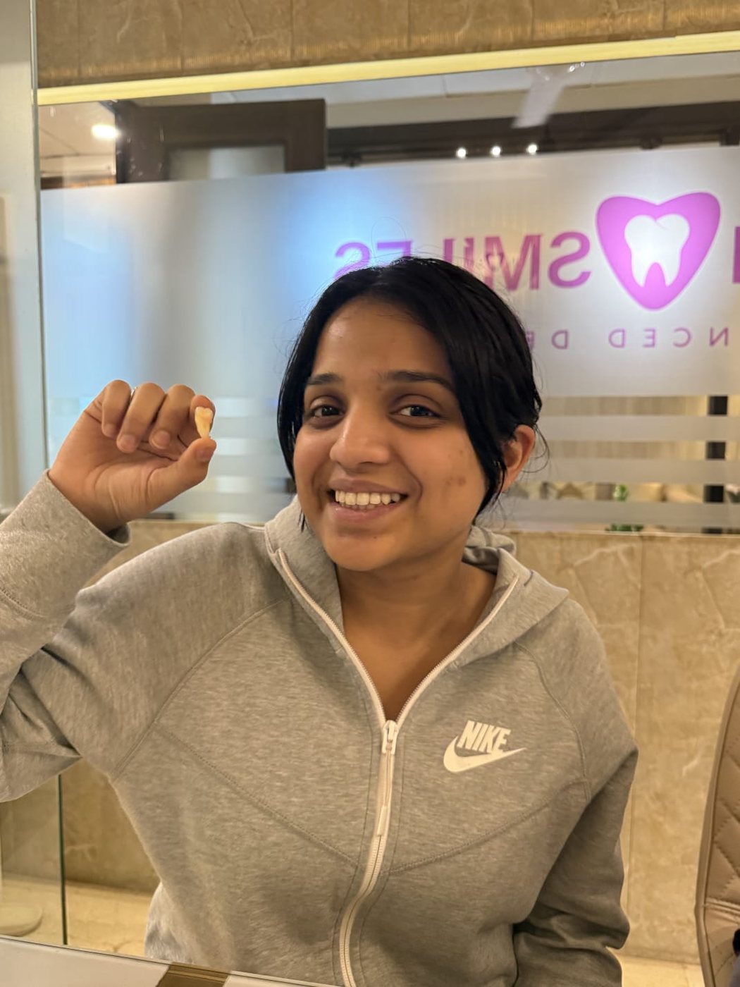 A smiling patient holding her extracted wisdom tooth